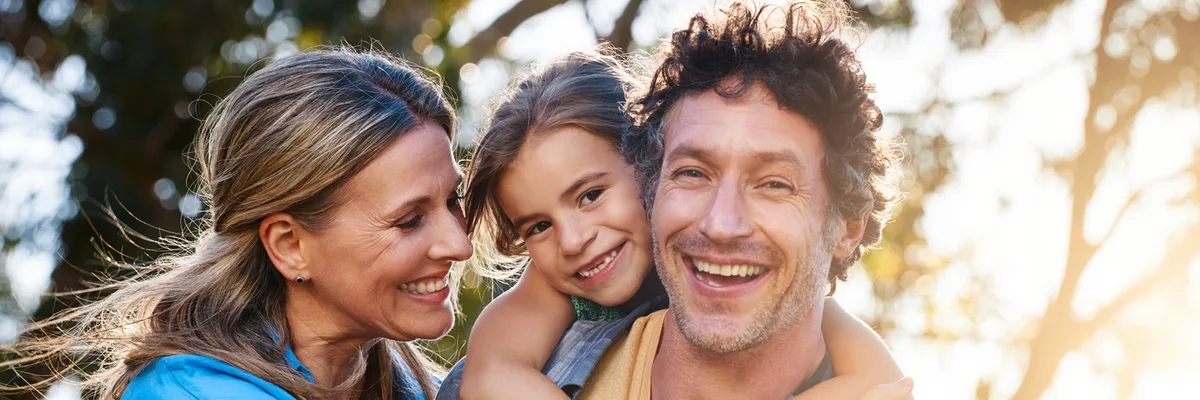 A mother, father and young daughter laughing together outdoors